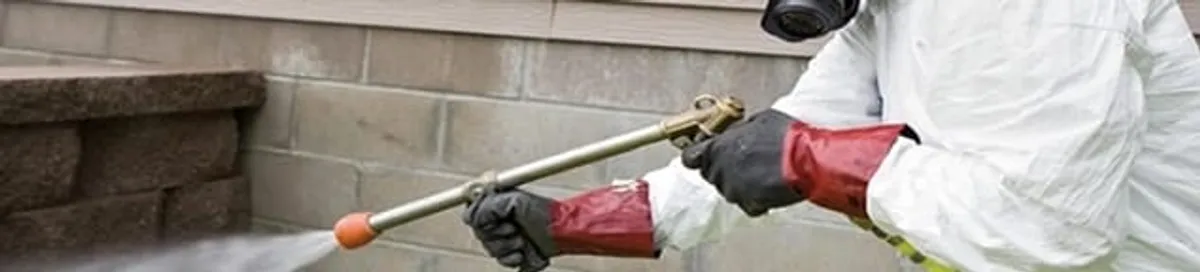 Pest control technician applying exterior insect treatment along a home foundation in Indianapolis, IN
