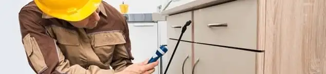 Roach exterminator applying treatment under kitchen cabinets in Indianapolis, IN