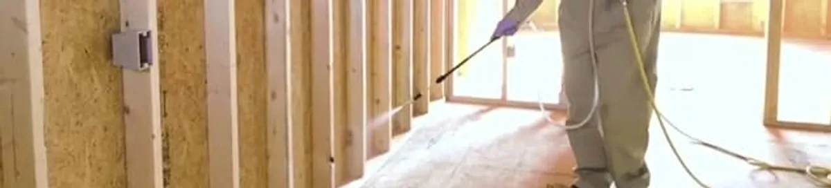 Termite treatment technician applying spray along framing and unfinished walls in Indianapolis, IN